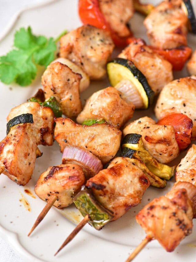 chicken skewers with vegetables on wooden sticks sitting on white plate.