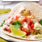 fish taco with lime and other toppings on white plate with text overlay 