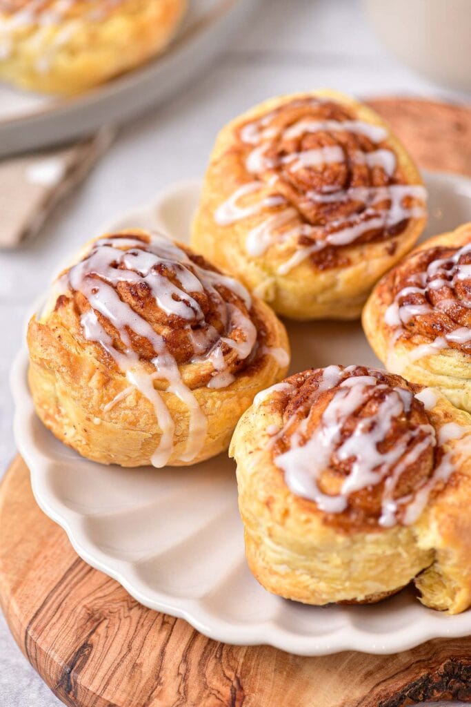 fluffy cinnamon rolls covered in icing on white plate sitting on wooden board.