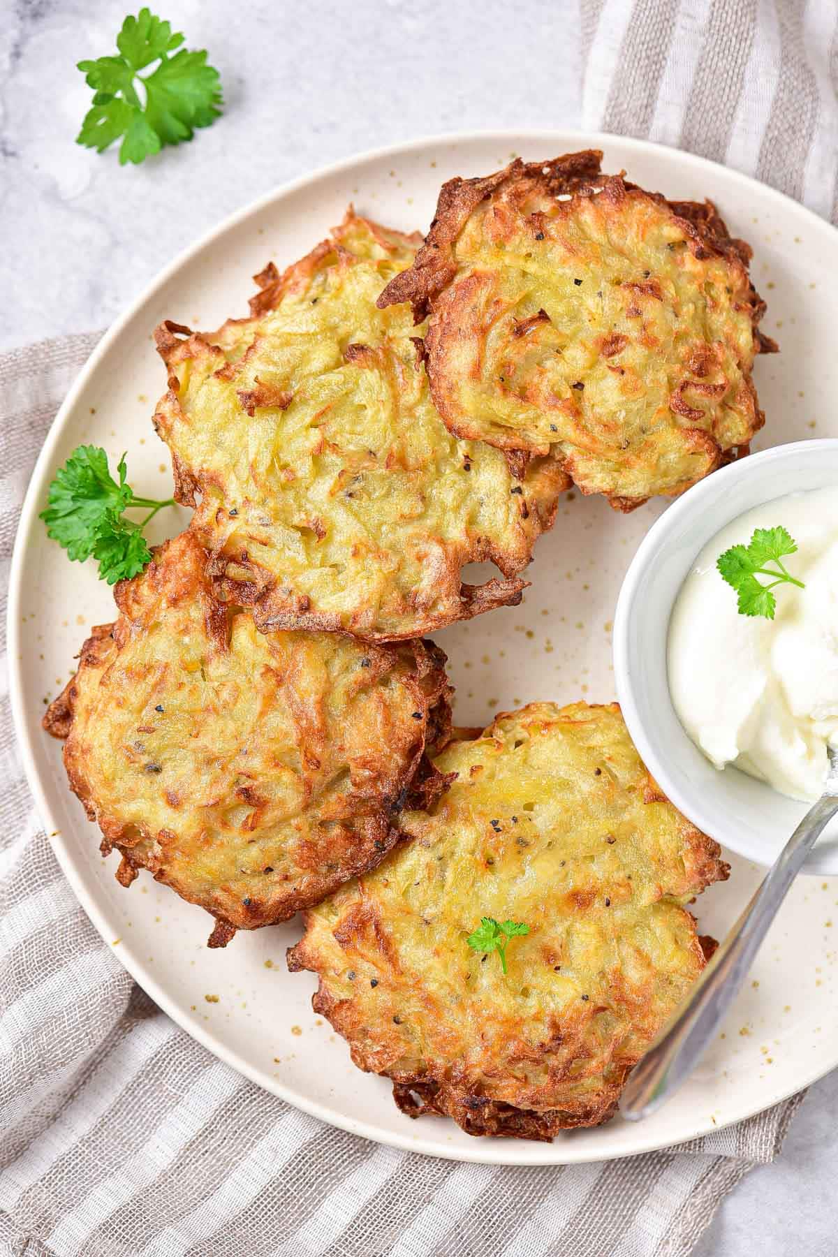 round crispy potato pancakes arranged on plate with smaller dish full of sour cream.