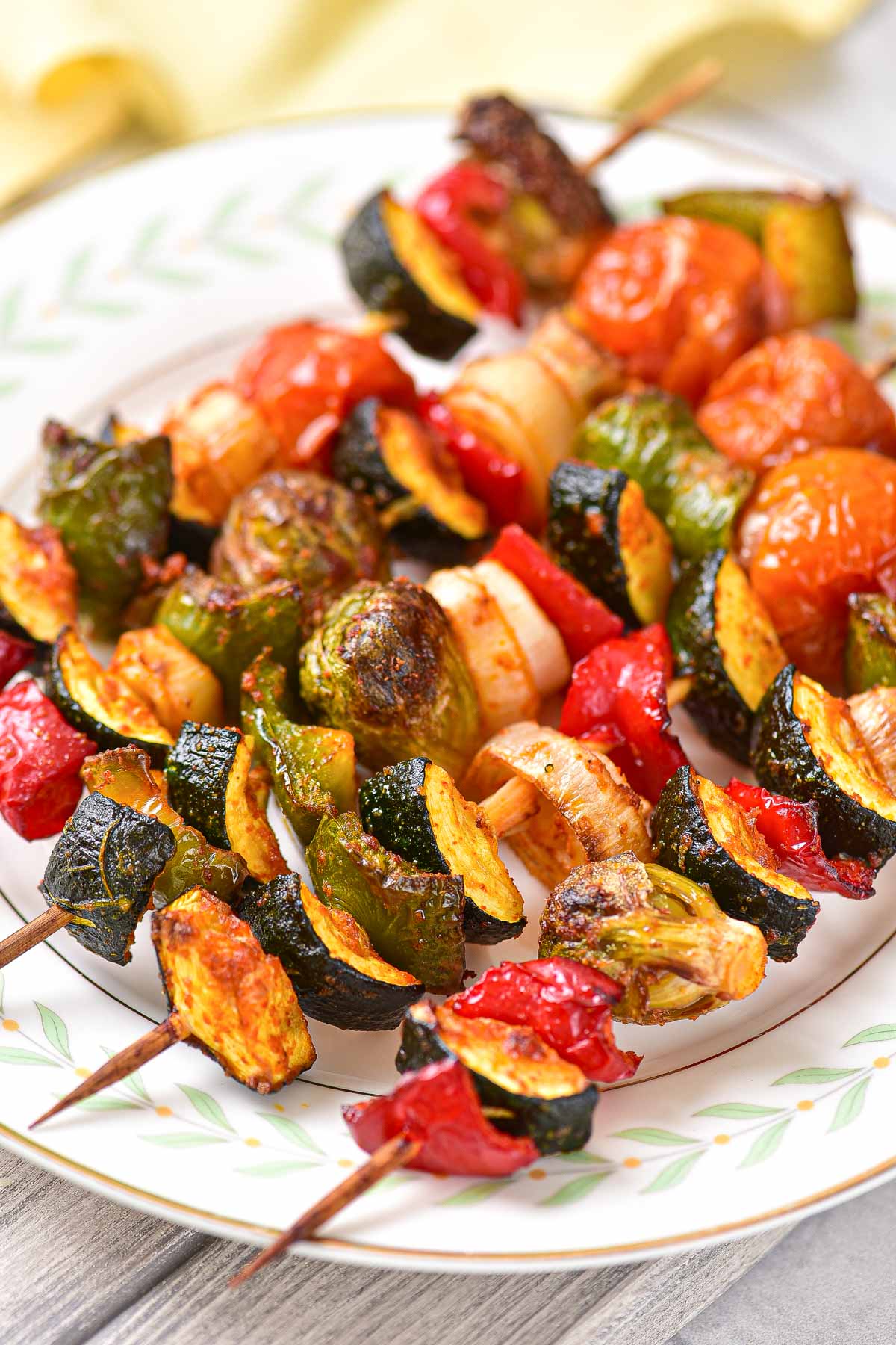 white plate with grilled vegetable skewers arranged in a row on top.