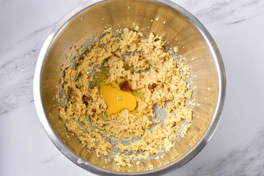 raw cookie dough batter in silver mixing bowl with cracked egg inside.