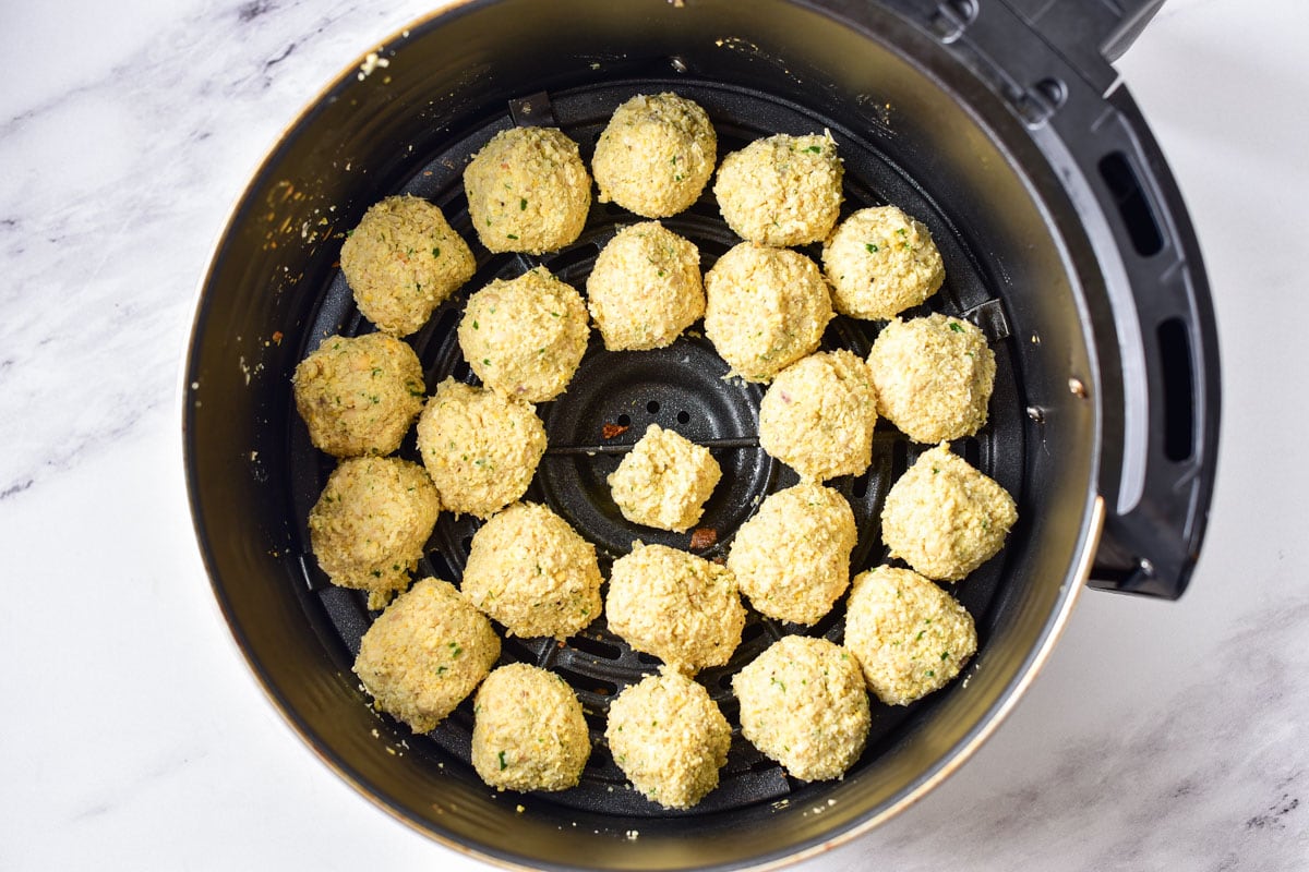 uncooked falafel balls arranged in circles in round air fryer basket.