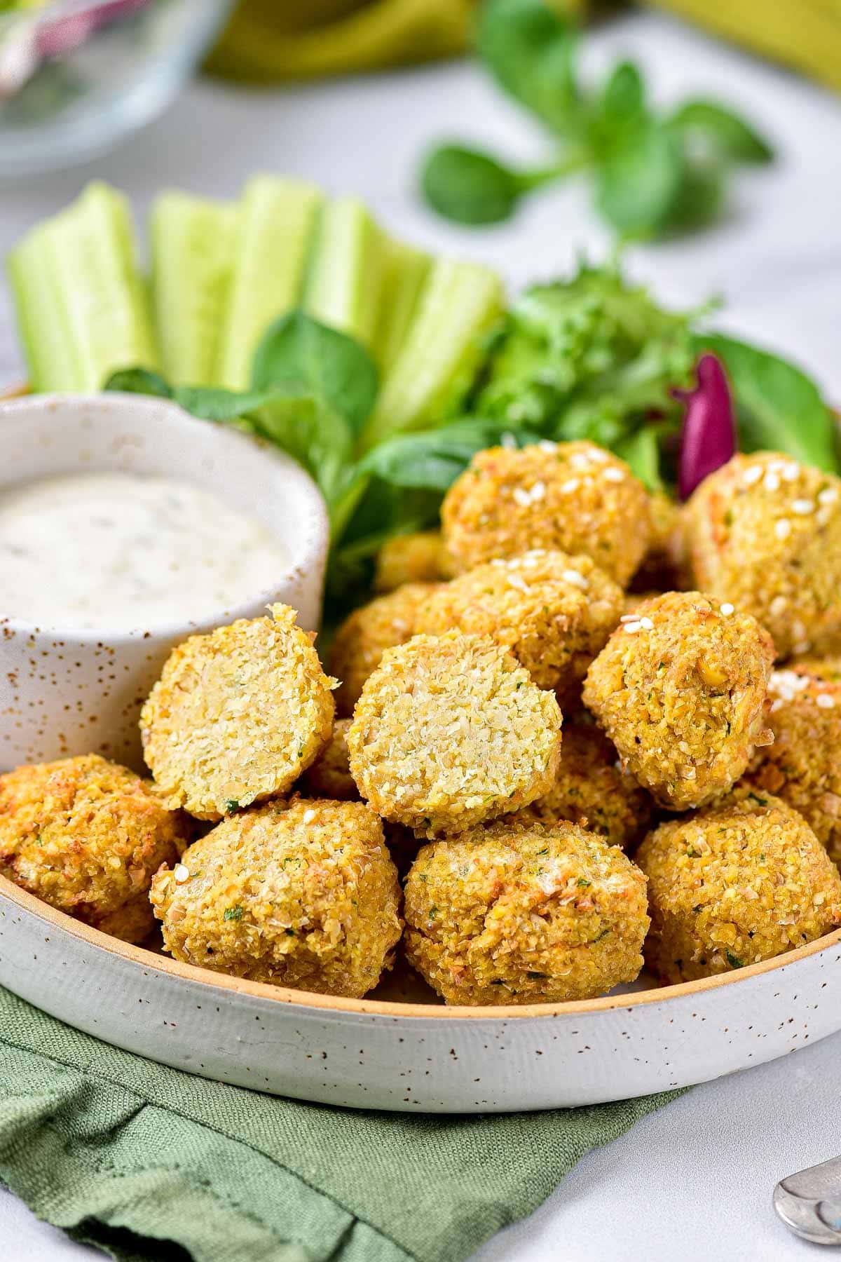 falafel ball cut in half sitting in pile of other falafel in bowl with sauce beside.