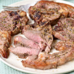 cooked lamb chops on white plate with fork behind.