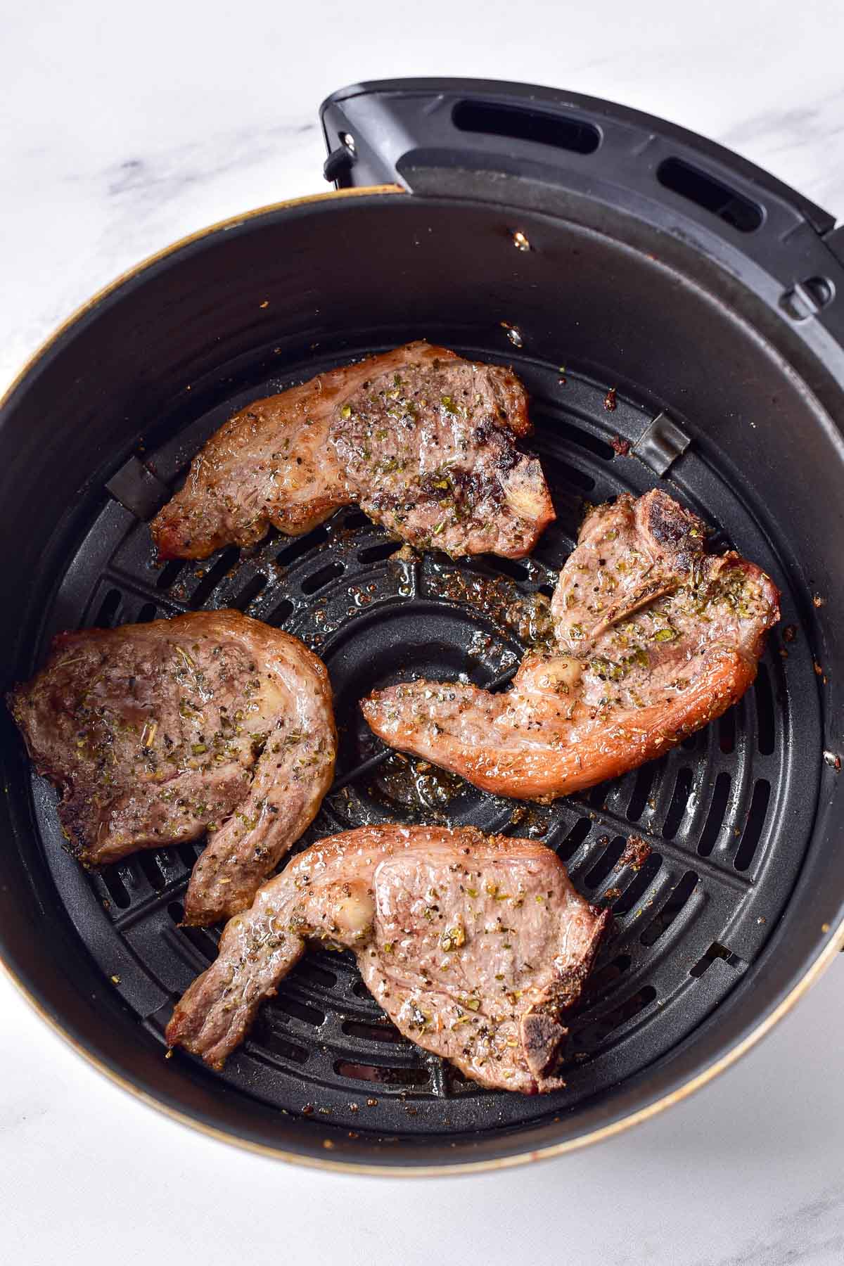 cooked lamb chops in round air fryer basket sitting in white counter.