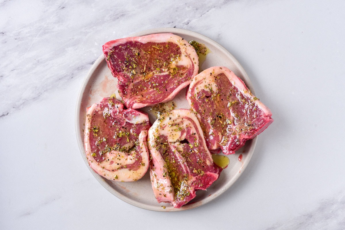 four raw lamb chops covered in spices on round plate sitting on counter.