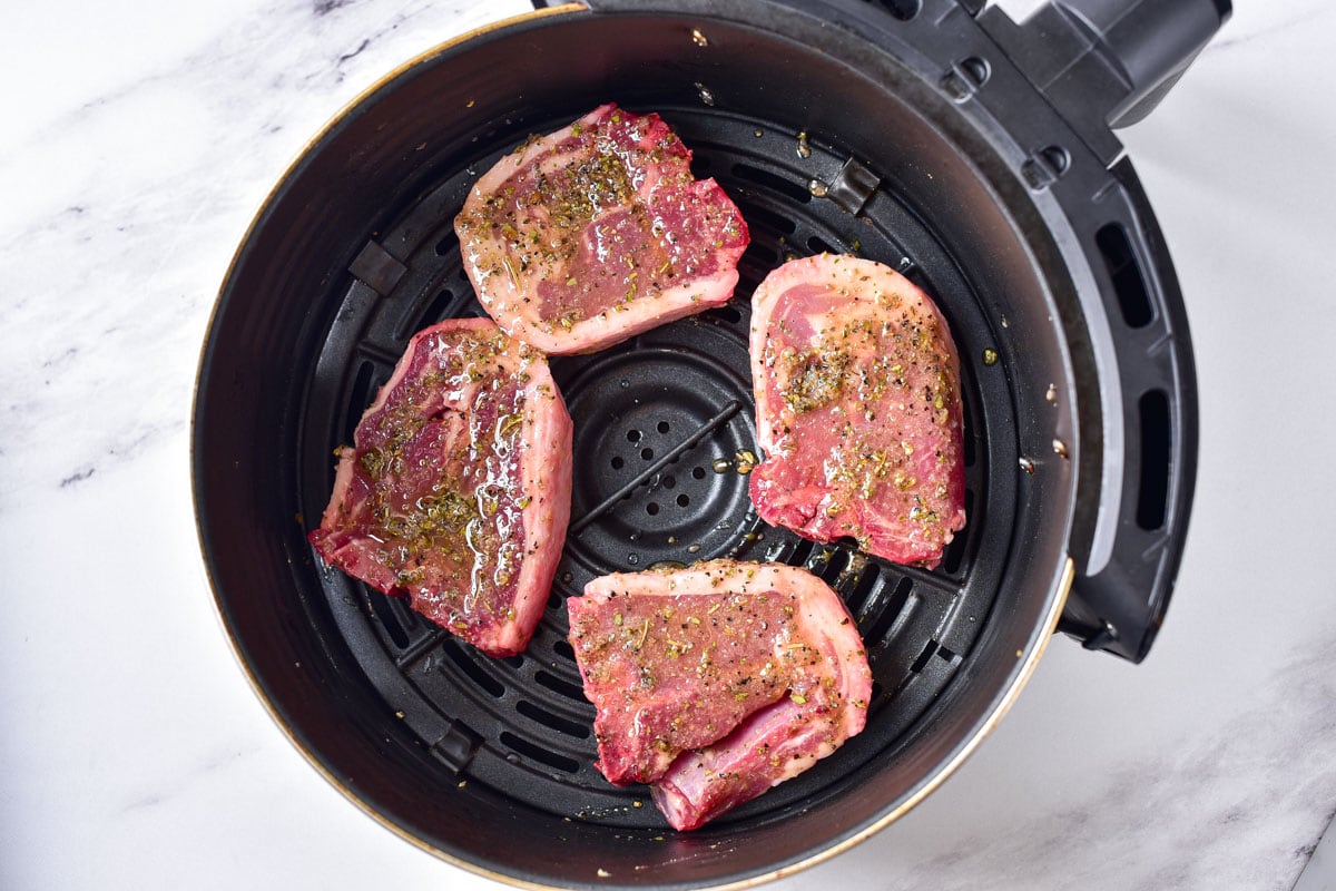 raw marinated lamb chops in round air fryer tray sitting on counter.