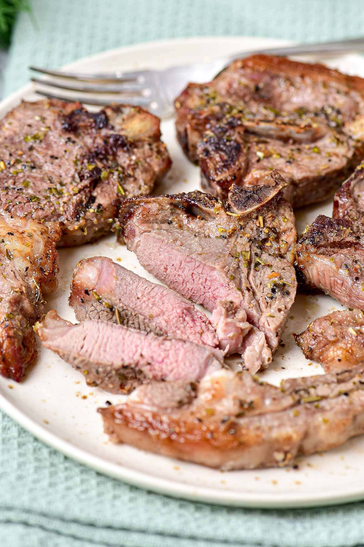 cooked lamb chops with pink centre placed on plate with silver fork behind.