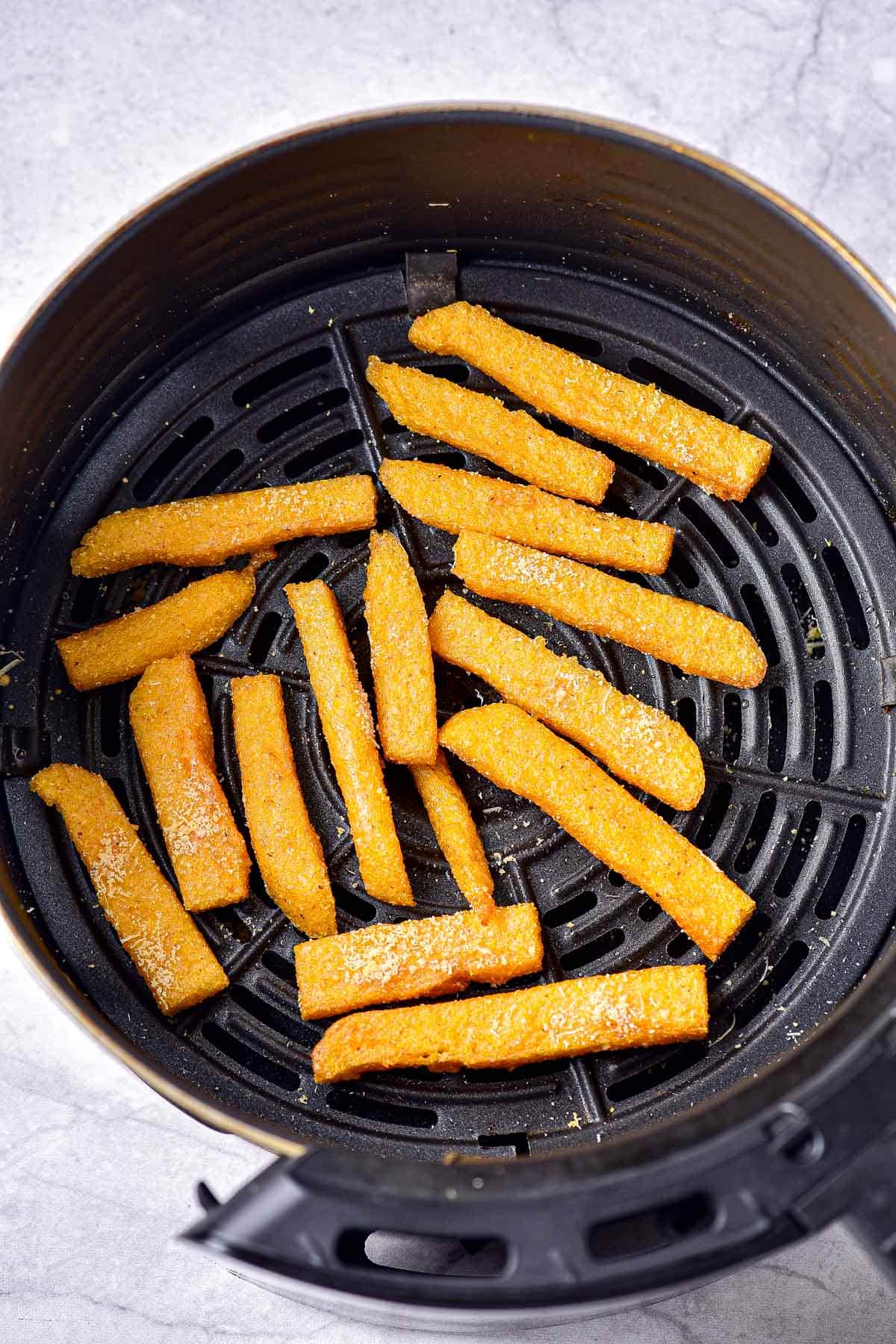 round black air fryer basket with cooked polenta fries inside.