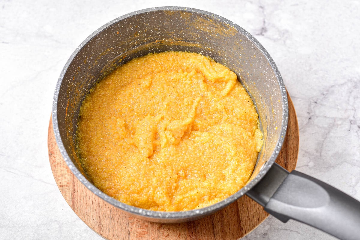 thickened polenta in a pot sitting on a round wooden board.