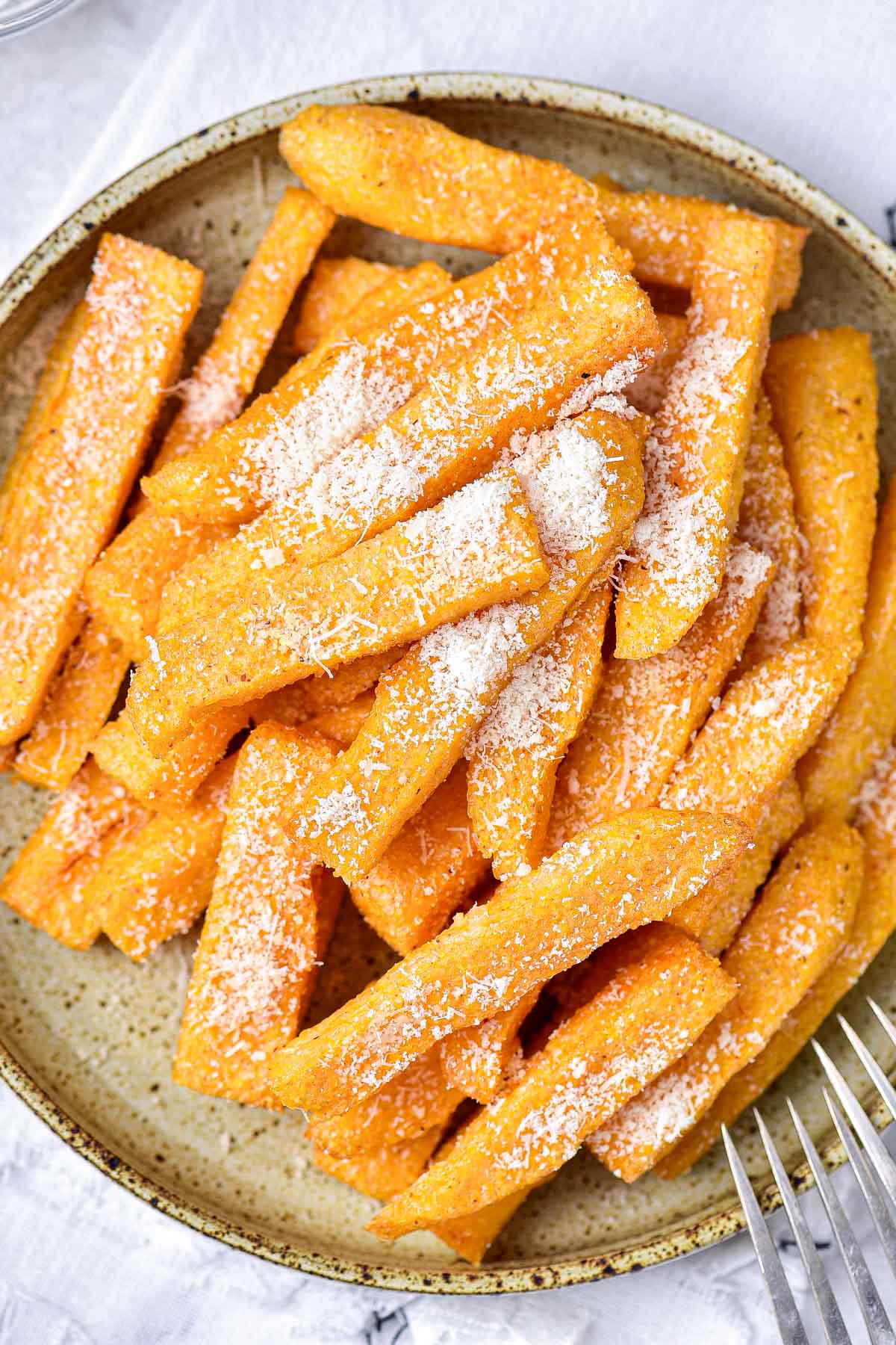 large plate of crispy polenta fries covered in shredded cheese.
