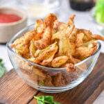 clear glass bowl of crispy potato peels on wooden board.