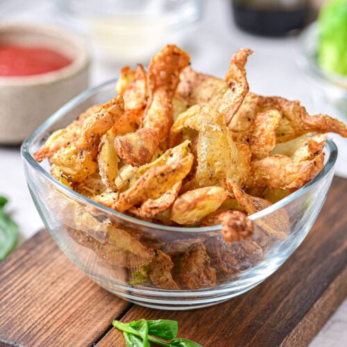 clear glass bowl of crispy potato peels on wooden board.