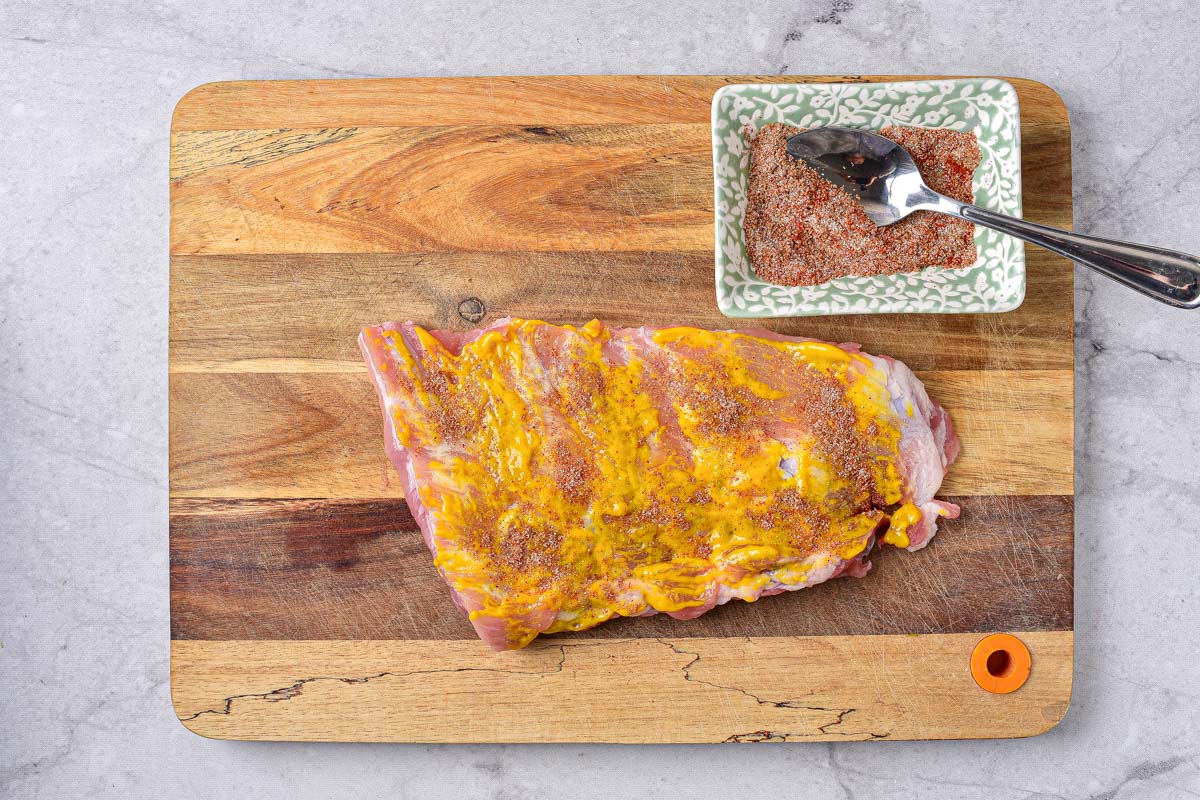 raw piece of rib on wooden board covered in dry rub spices.