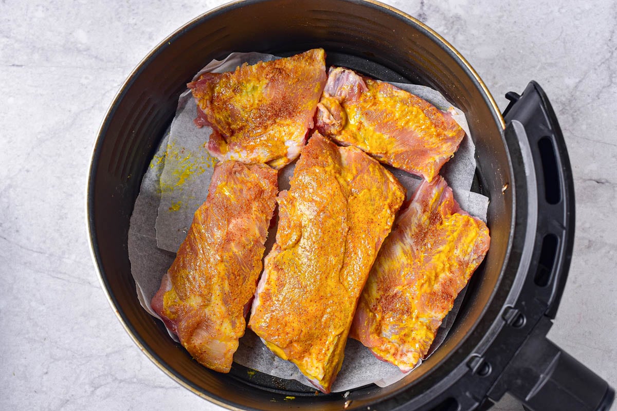 raw pieces of dry marinaded ribs in round air fryer basket.