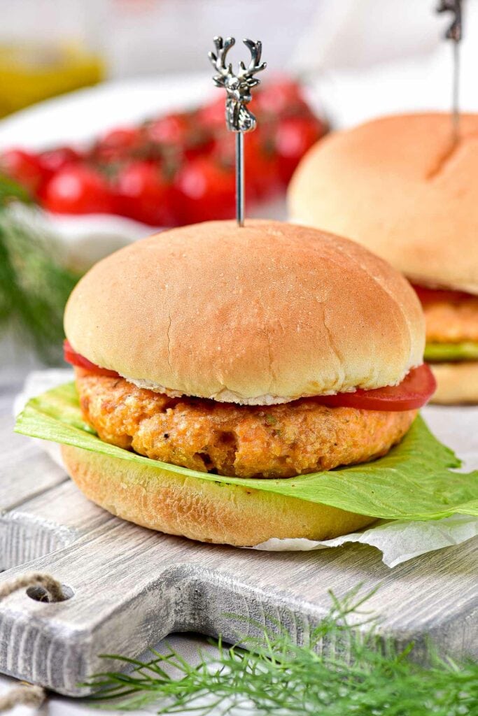 salmon burger dressed on hamburger bun with lettuce and tomato sitting on wooden board.