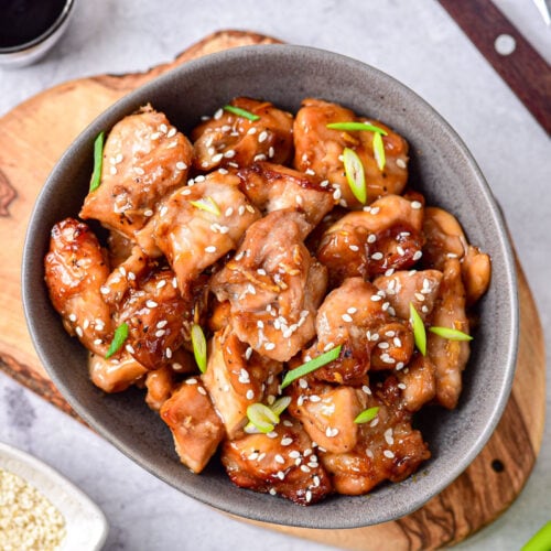 grey bowl of chicken teriyaki with sesame seeds and green onion on top.