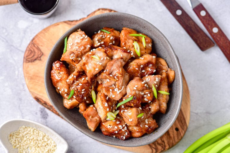 grey bowl of chicken teriyaki with sesame seeds and green onion on top.