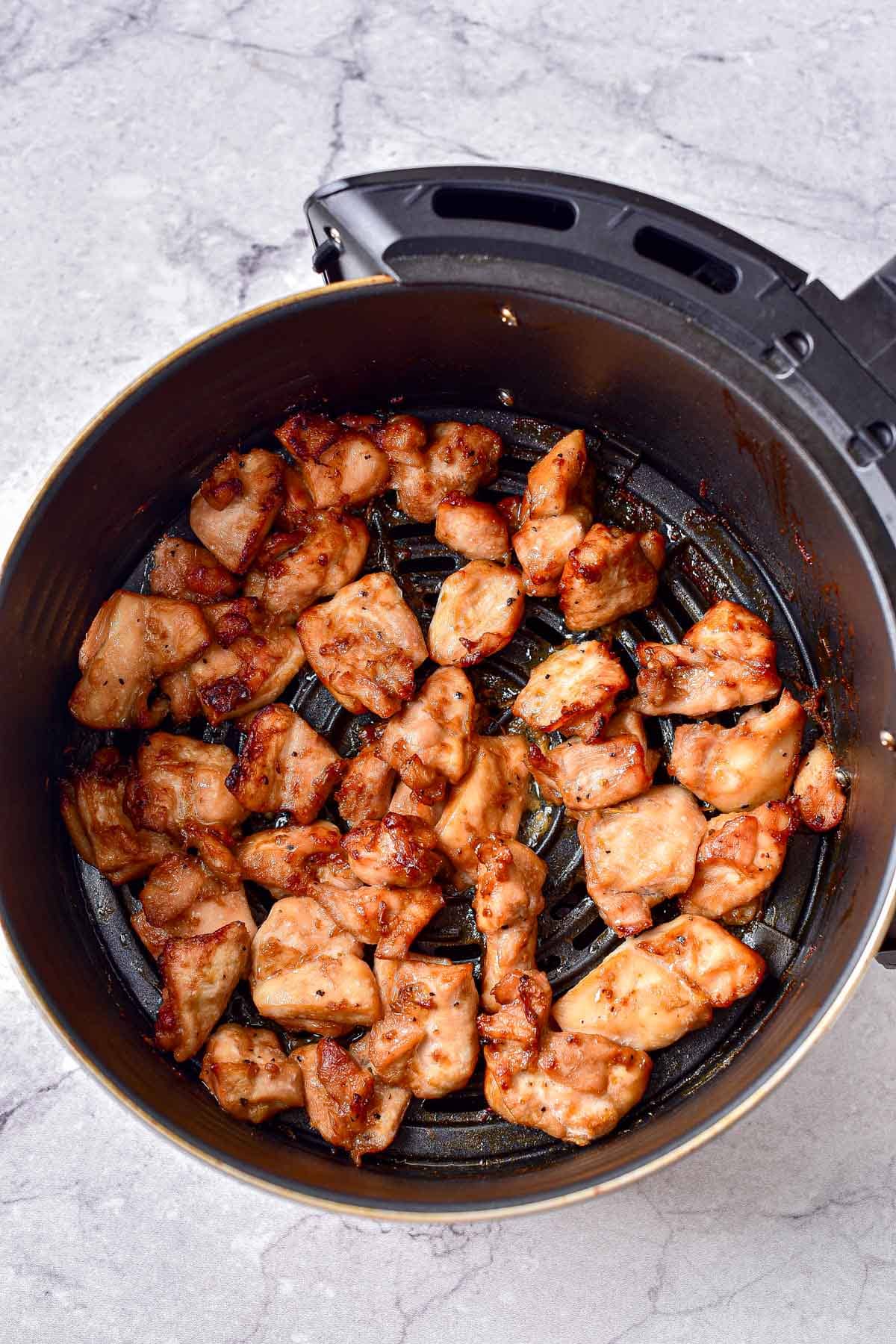 cooked pieces of teriyaki chicken in round black air fryer basket with counter around.