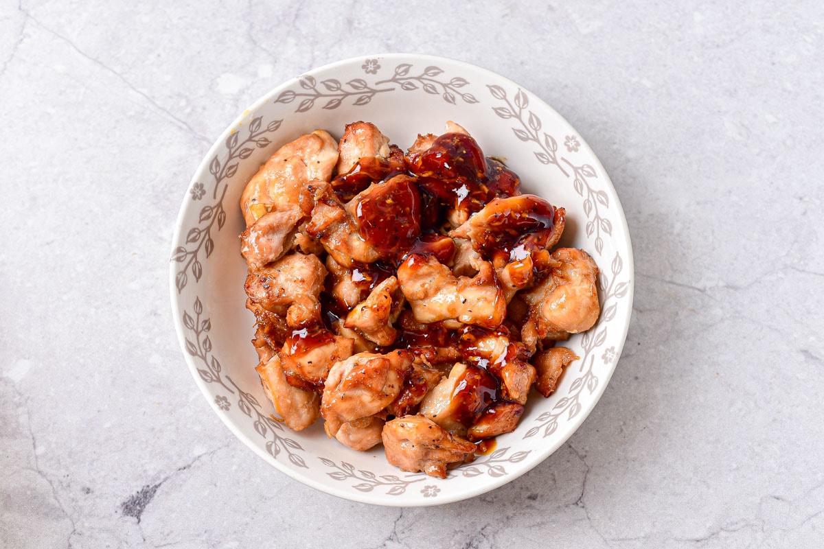 white bowl of cooked teriyaki chicken with more sauce added on top.