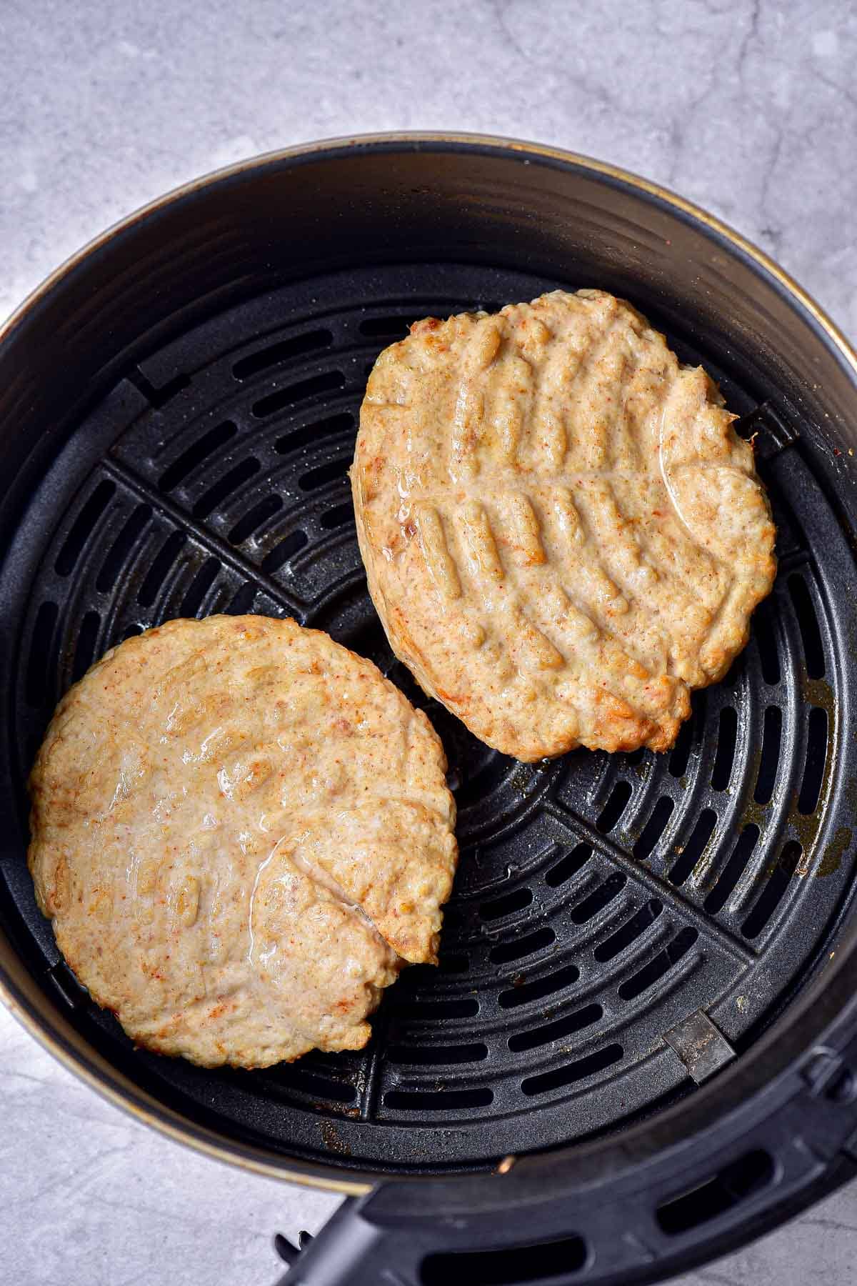 cooked turkey burger patties in round black air fryer tray on counter.