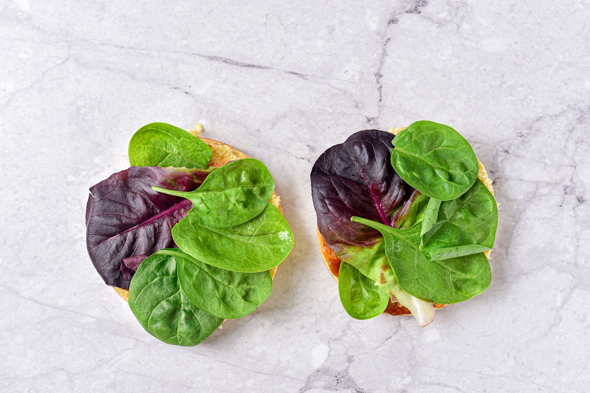 two burger buns on marble counter covered in lettuce and spinach.
