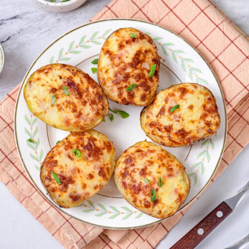 five crispy baked potato halves on white plate with napkin underneath.