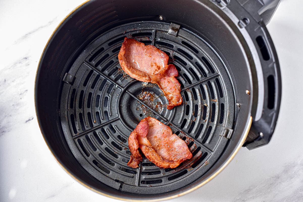 two cooked pieces of bacon in round black air fryer basket.