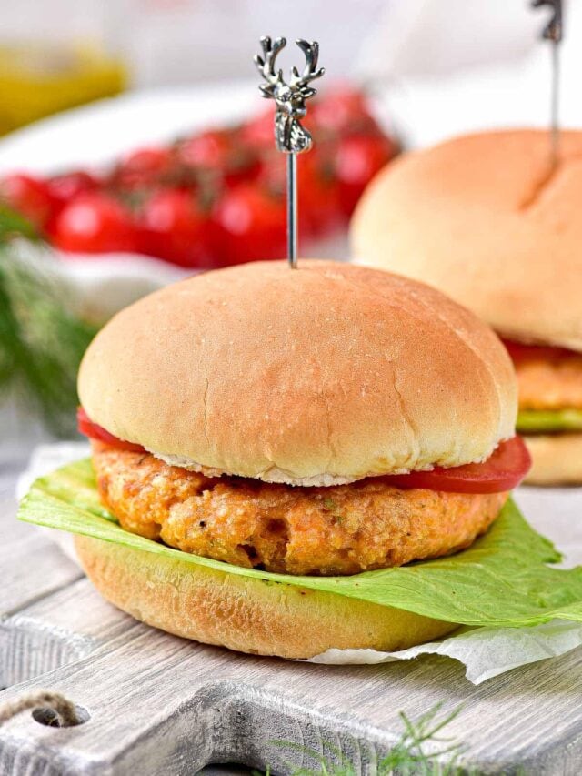 salmon burger dressed on hamburger bun with lettuce and tomato sitting on wooden board.