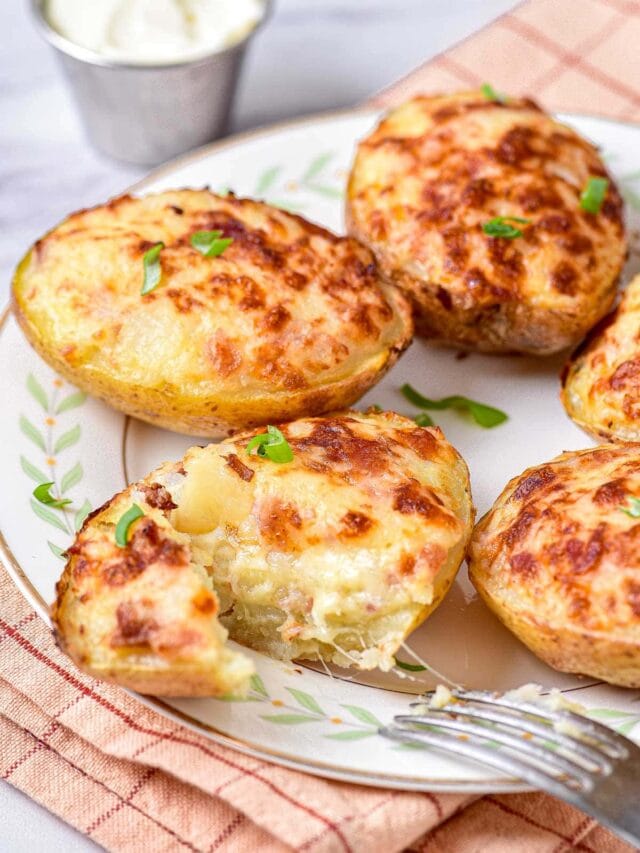 baked potato topped with golden brown cheese on plate with green onion around.