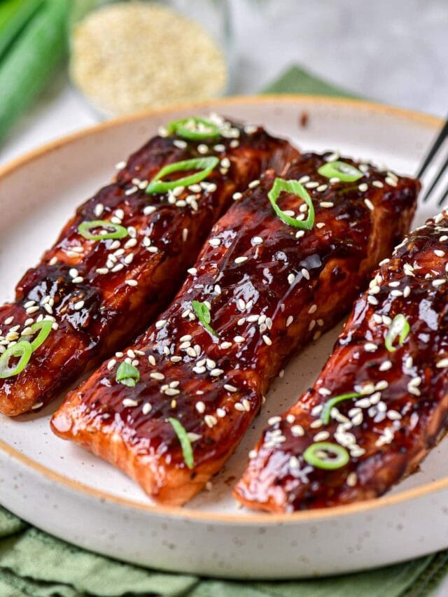 three teriyaki salmon pieces covered in green onion and sesame seeds on plate.