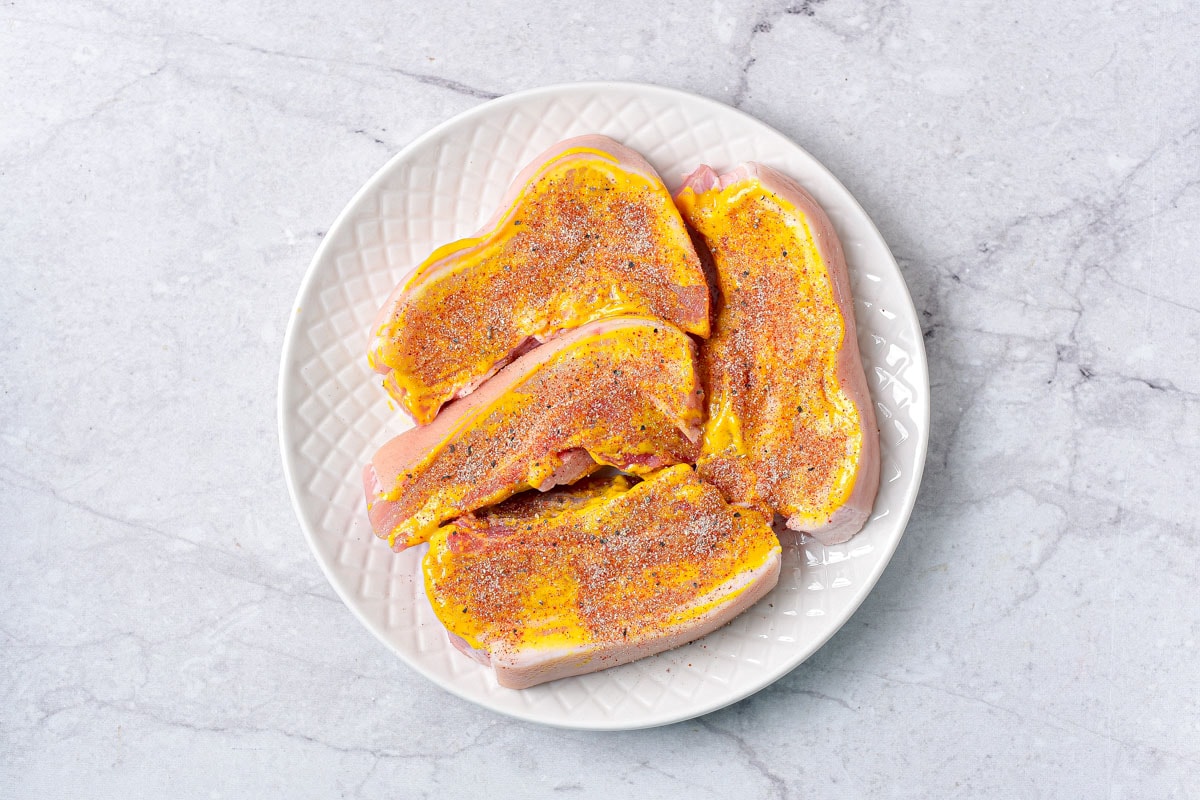 raw pork belly covered in mustard and spices sitting on plate.