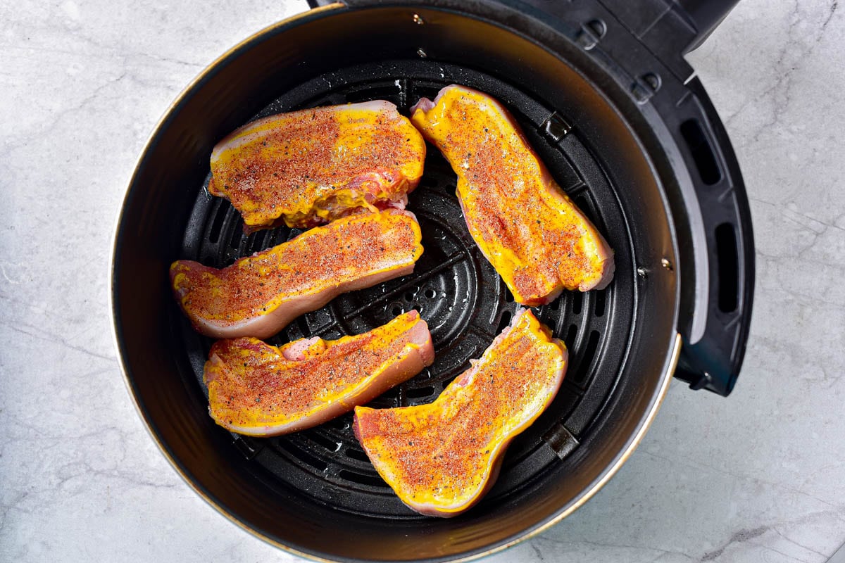 raw pork belly pieces laying on round air fryer basket on counter.