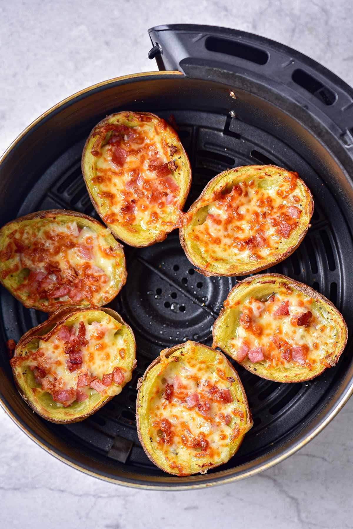cheesy crispy potato skins in round black air fryer tray.
