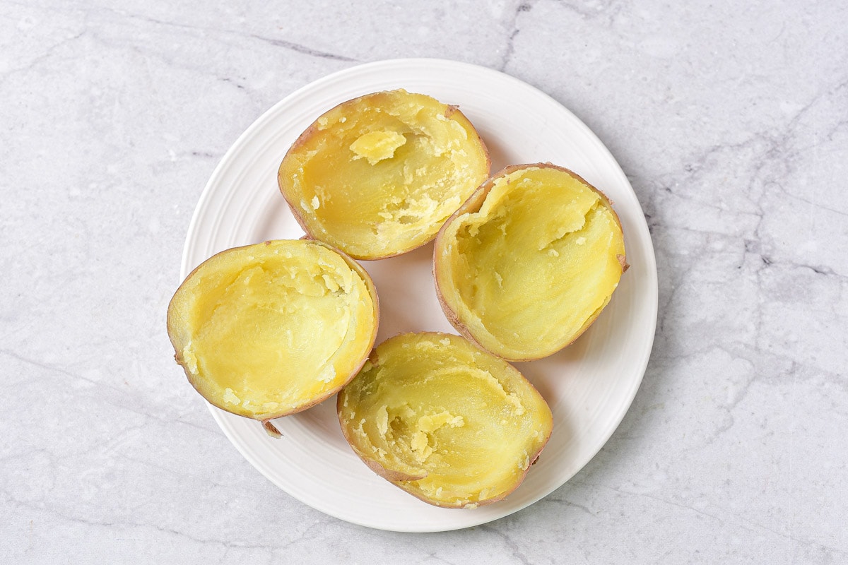 four potato halves with potato scooped out on a white plate on counter.