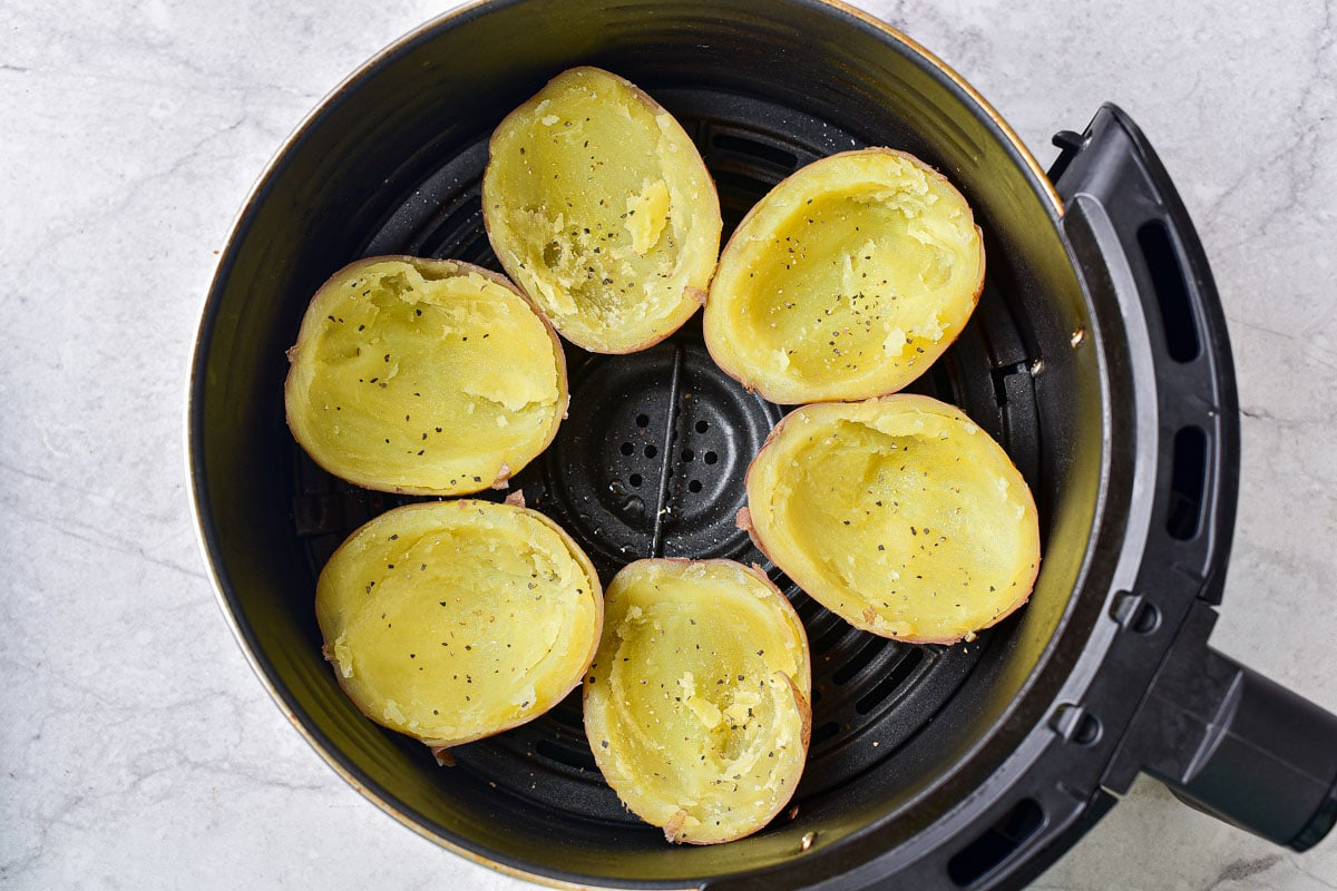 six halves of potatoes with flesh scooped out in round black air fryer basket.