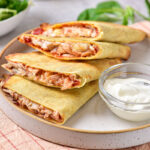 sliced quesadilla on plate with bowl of sour cream beside.