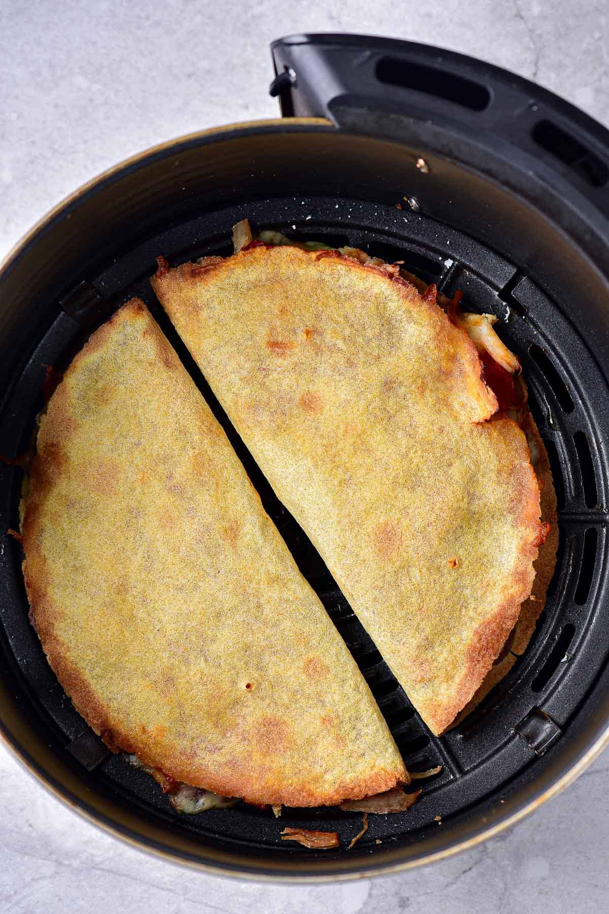 two crispy quesadillas in round black air fryer tray on counter.