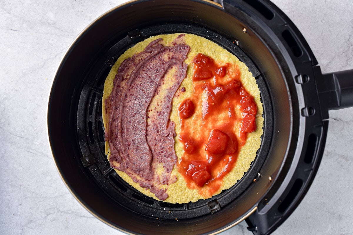 corn tortilla in air fryer basket covered half in beans and half in salsa.