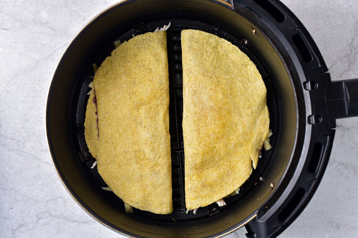 two round tortillas folded in half and stuffed with ingredients sitting in round air fryer tray.
