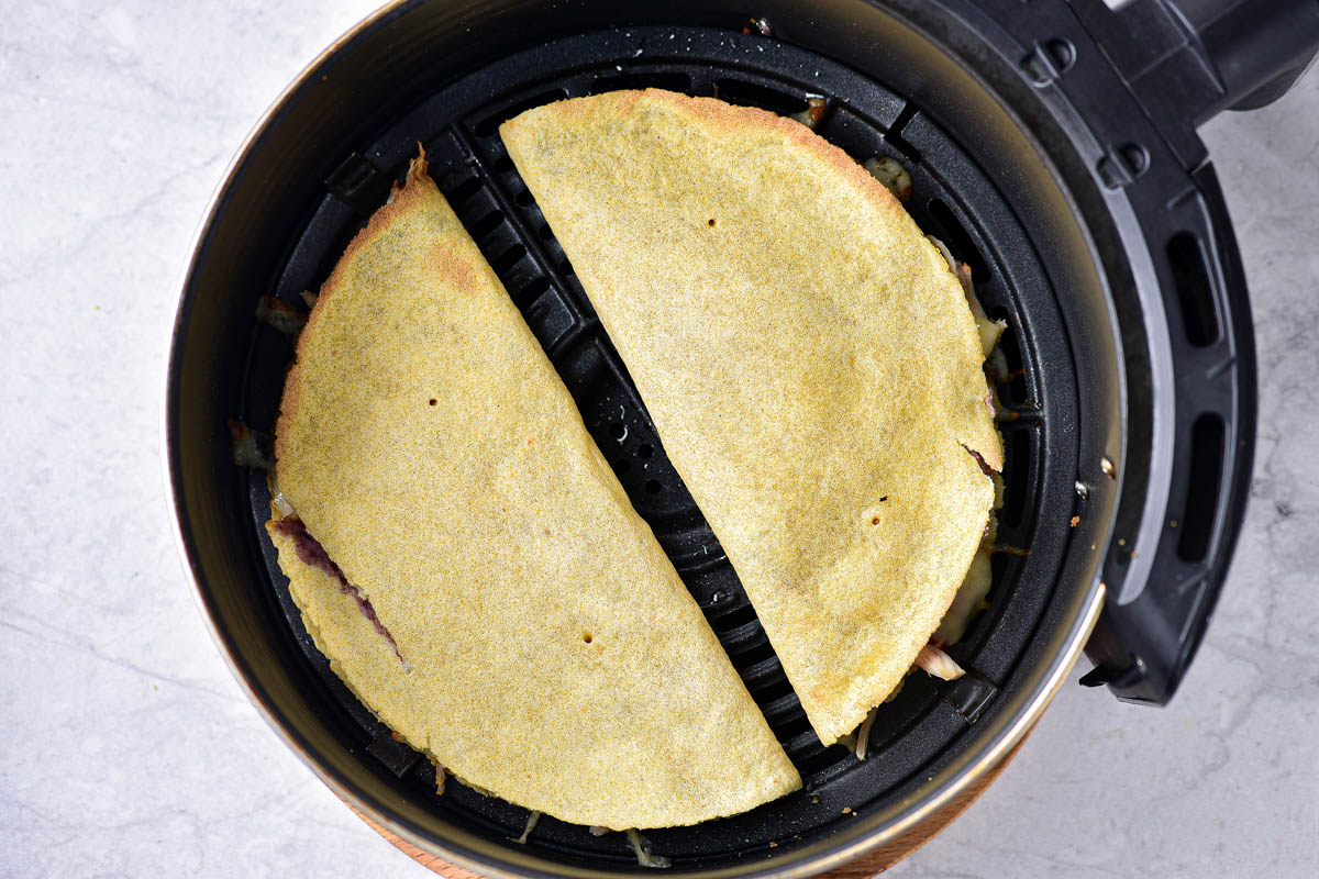 two quesadillas in round black air fryer tray on counter.
