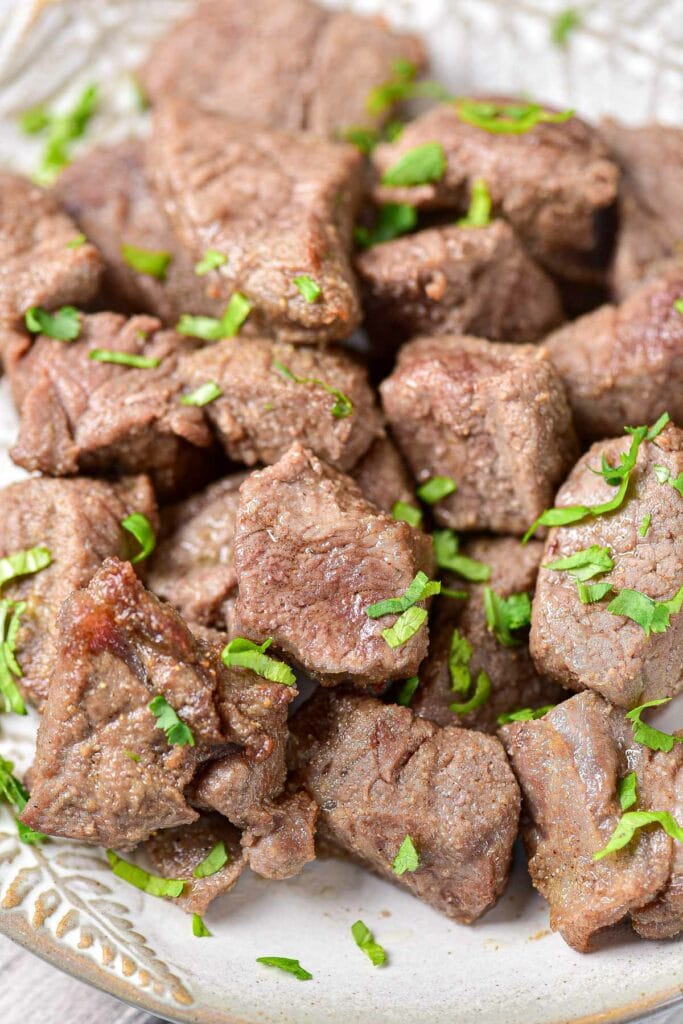 cooked steak bites covered in chopped parsley on plate.
