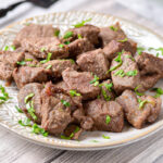 steak bites covered in chopped parsley on white plate.