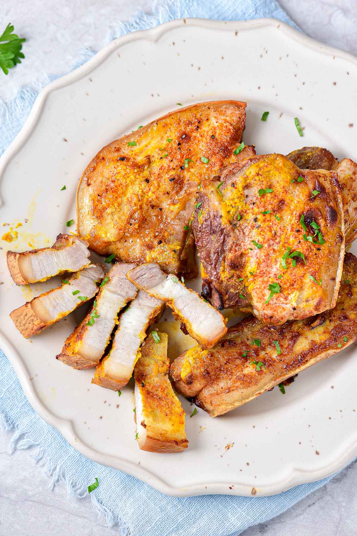 strips of marinated pork belly on plate covered in chopped parsley.
