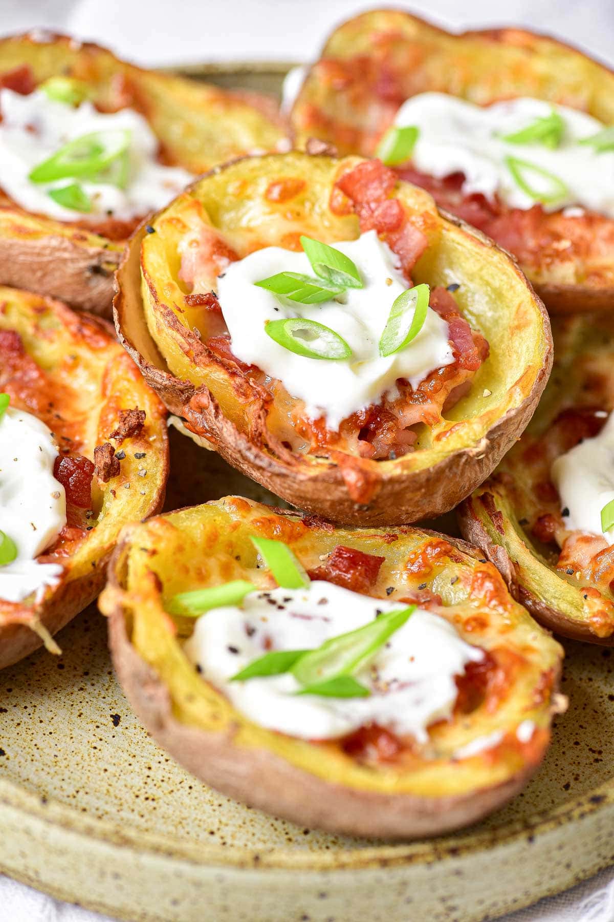 air fryer potato skins with sour cream and green onion on top stacked on plate.