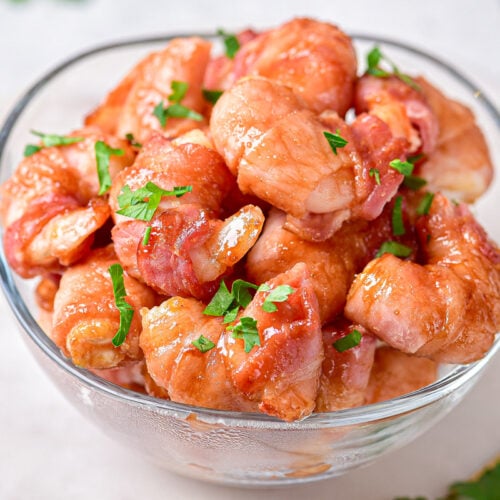 glass bowl filled with bacon wrapped shrimp covered in green herbs.