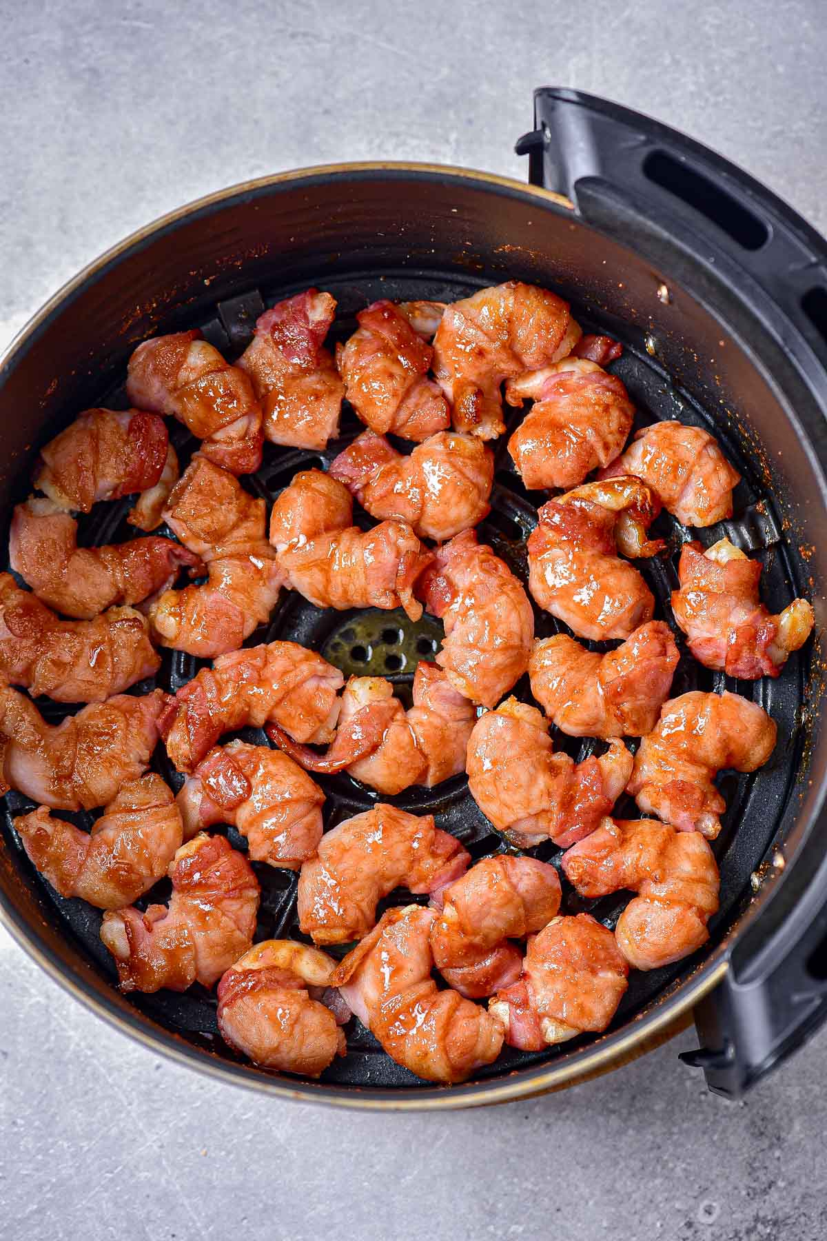 cooked bacon wrapped shrimp in round black air fryer basket.