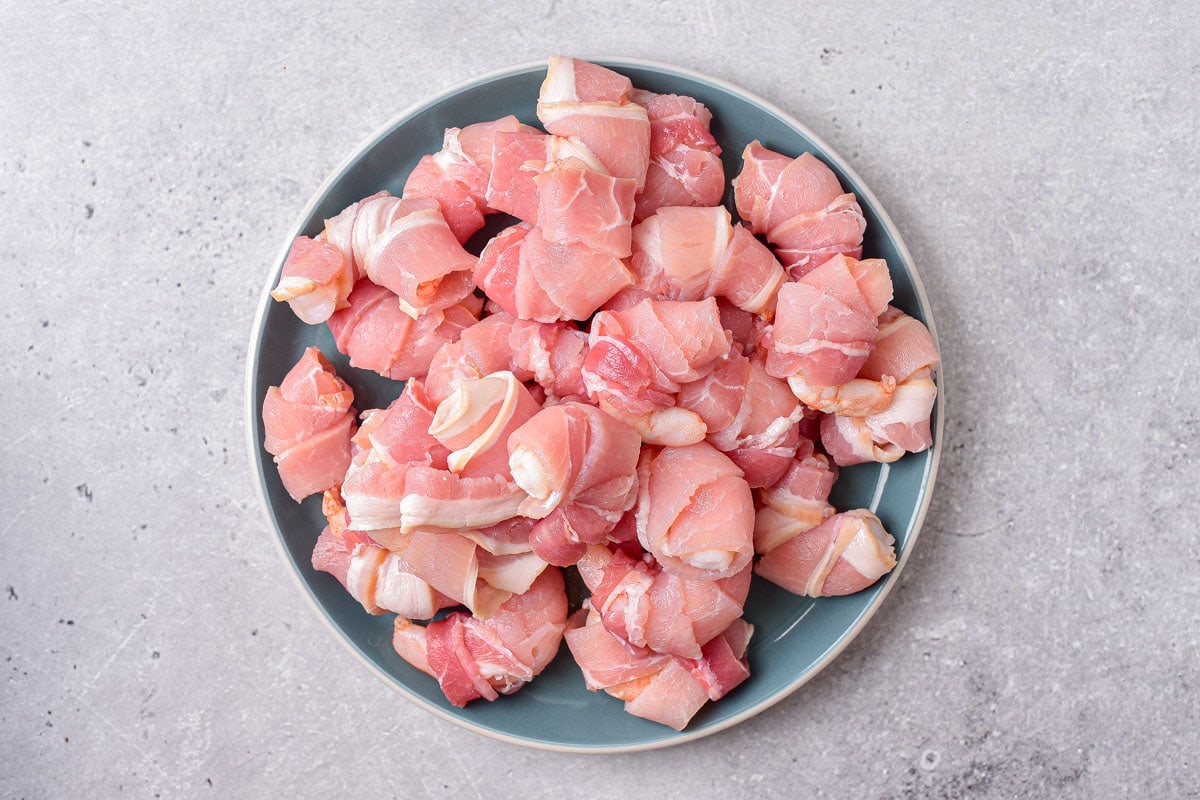 plate of shrimp wrapped in raw pieces of bacon with counter top around.