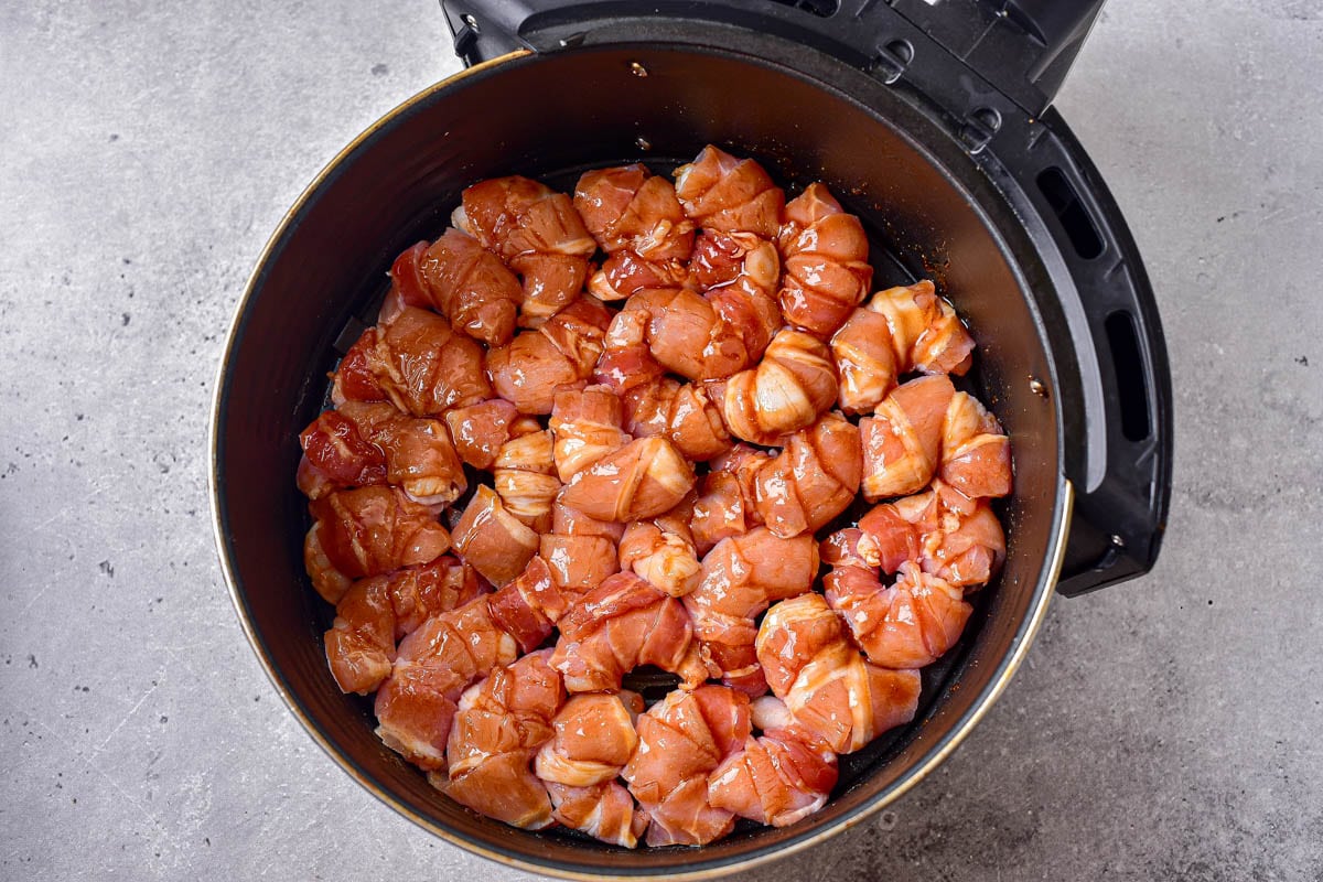 bacon wrapped shrimp in black round air fryer basket on counter.